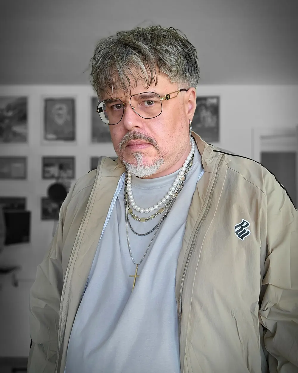 Marko Leicht in a light jacket with pearl necklaces in front of a wall of pictures